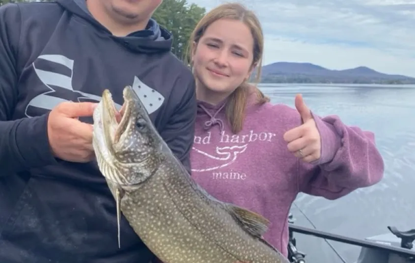 A man and woman hold a large fish and give a thumbs up.