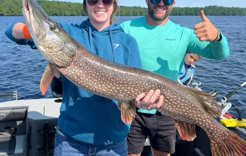 Two people holding a giant pike while giving thumbs up.