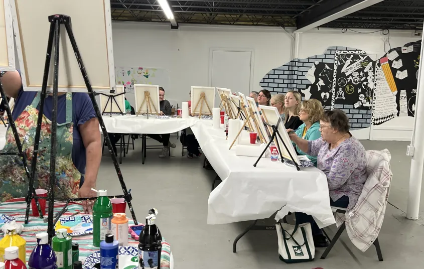 People at a long table painting on canvases.