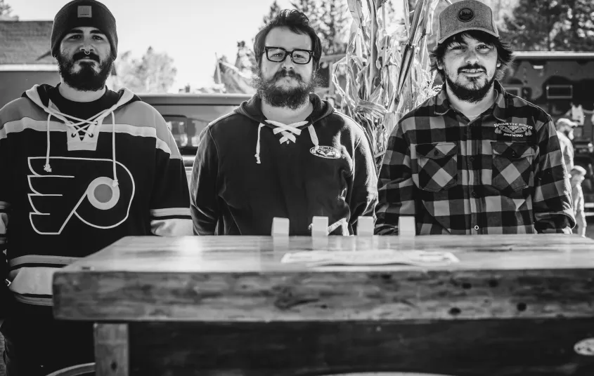 Three men display Raquette River Brewing merch