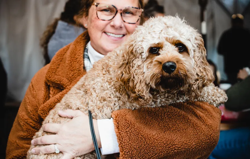 A smiling lady holds her medium sized blonde dog in this pet friendly establishment.
