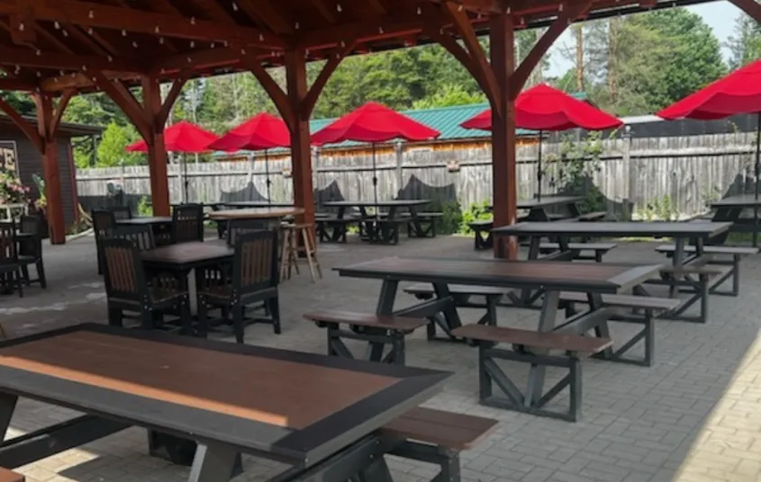 Rows of picnic tables under the covered roof of the brick patio at Raquette River Brewing.
