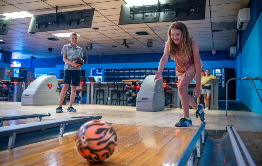A girl throws a bowling ball with flame decor down the lane.