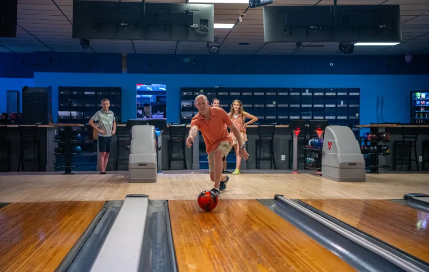A man sends a bowling ball down the polished lane.