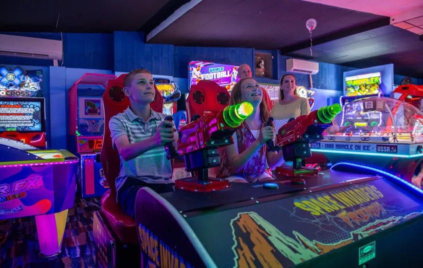 Kids play an arcade game surrounded by black light colors.