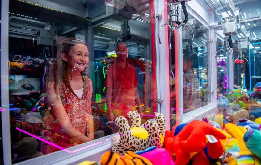 A girl uses the the claw machine for a prize.
