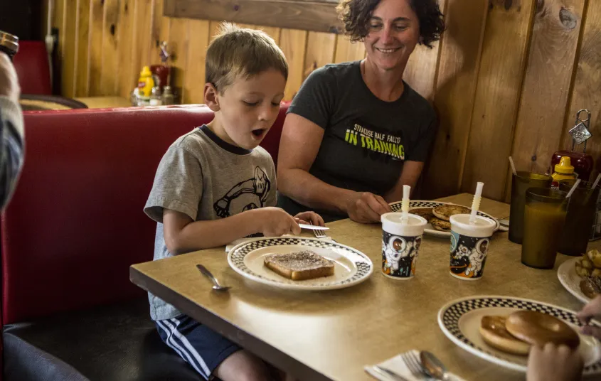 A smiling family enjoys a meal in a booth.