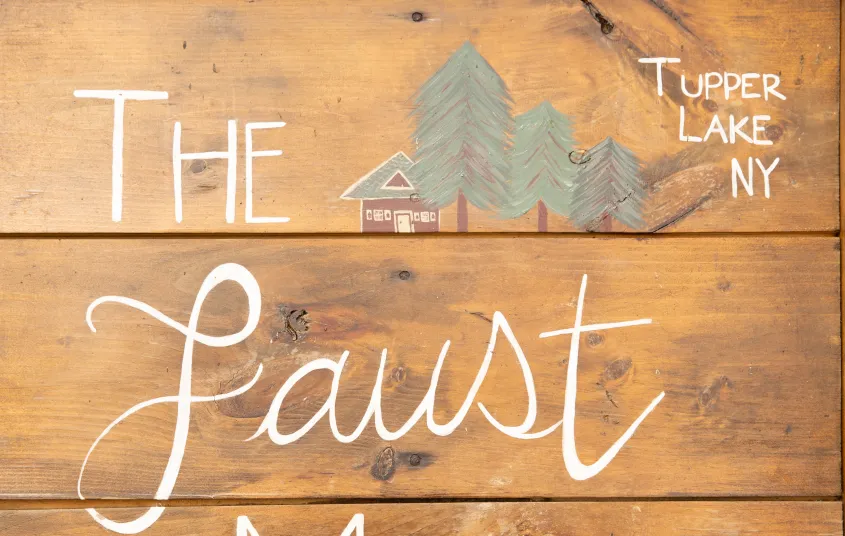 A wooden sign with white lettering The Faust Motel Tupper Lake NY