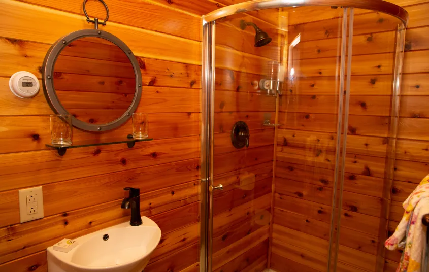 The horizontal wood paneling in the bathroom with small white sink and large curved clear shower.