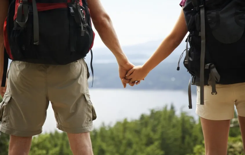 Two people hold hands while looking out over pine trees and a lake