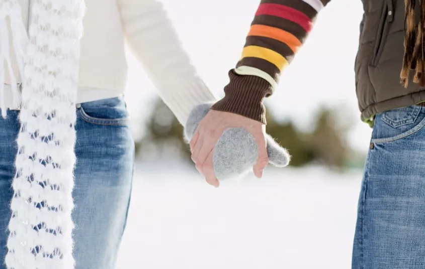 Two people holding gloved hands and walking in the snow