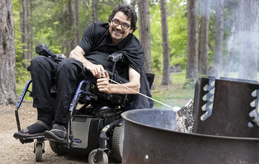 A man in a wheelchair roast a marshmallow.
