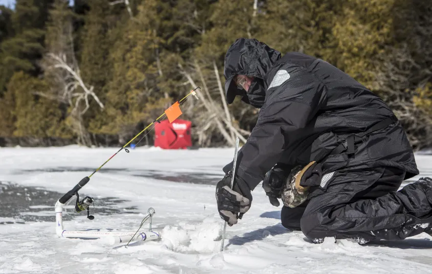 An ice fisher cutting a hold in the ice