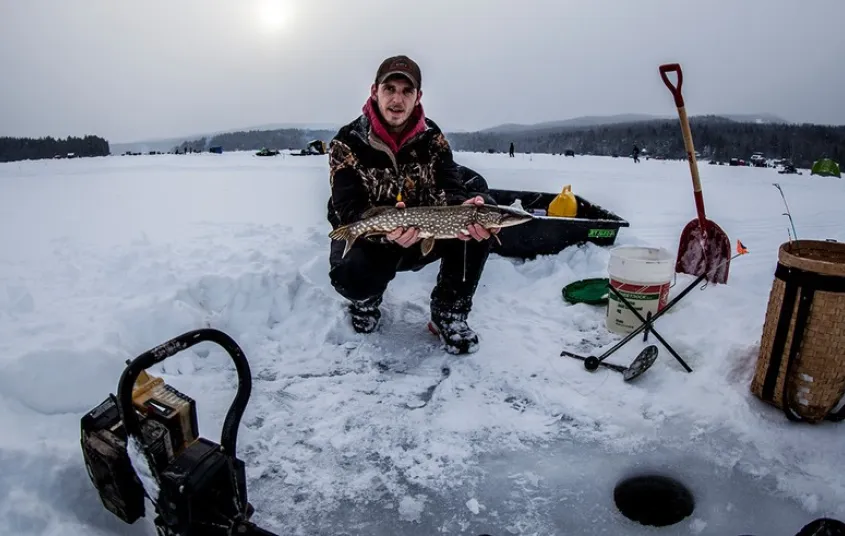 A guy holding up a fish during the winter