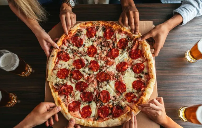 Lots of hands reach to pull a slice of pizza