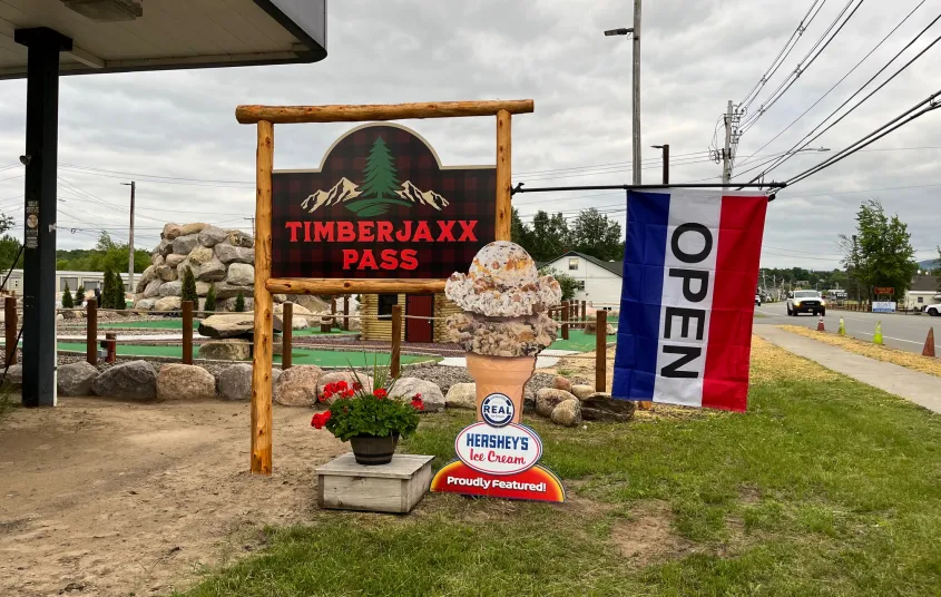 Timberjaxx Pass Ice Cream and Mini Golf shop Tupper Lake Sign with open flag.