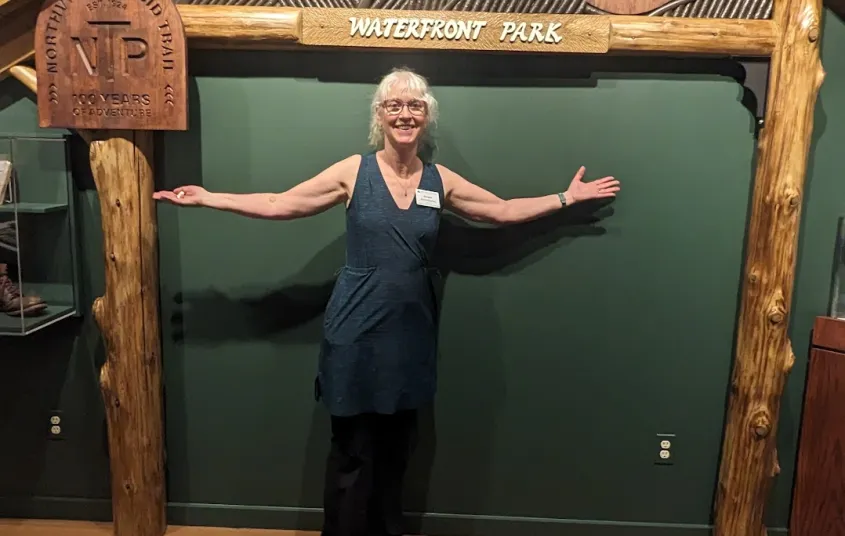 A woman smiles under a wooden arch against a green wall where plaques describing the NPT are displayed