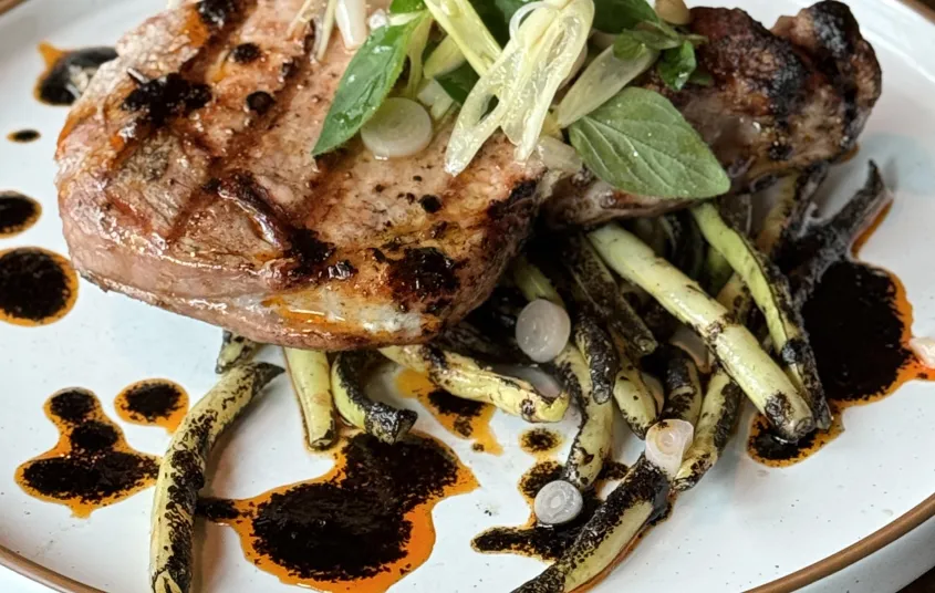 A perfectly grilled pork chop with seasoned wax beans