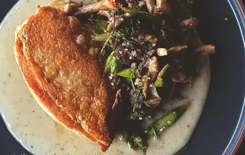 A pan fried chicken thigh with mushroom side dish over cream base.