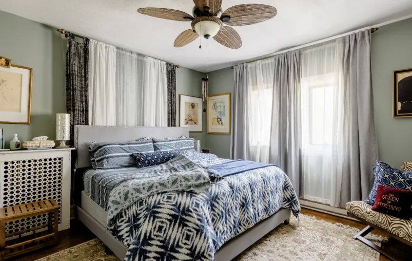 A guest bedroom with large bed floor to ceiling window treatments and light accents.