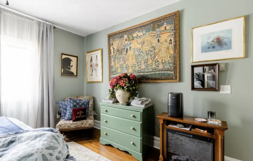 A guest bedroom with electric fireplace and wingback chair.