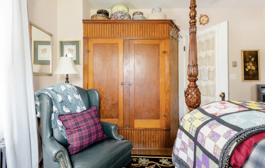 large wooden wardrobe with a leather wingback chair in a guest room