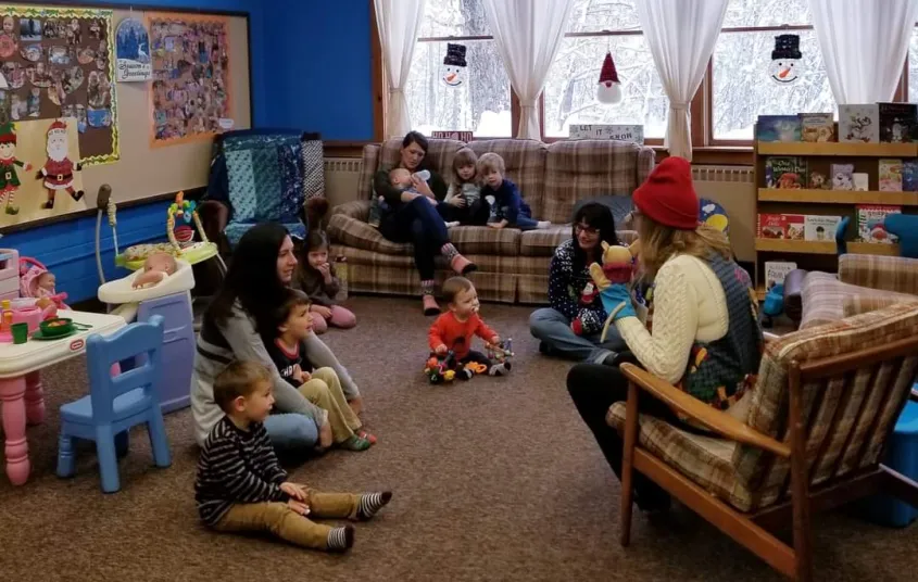 Families sit on the carpet and couches at story time.