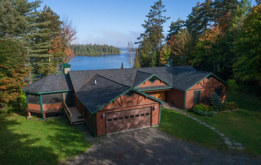 An aerial view of a cabin by a lake surrounded by tall pines.