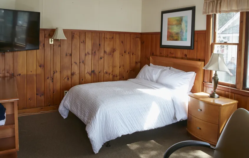 Plush white linens on a queen bed in a wood paneled room at The Ashley.
