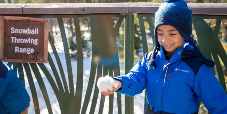 A young child gleefully looks down at his hand holding a freshly made snowball