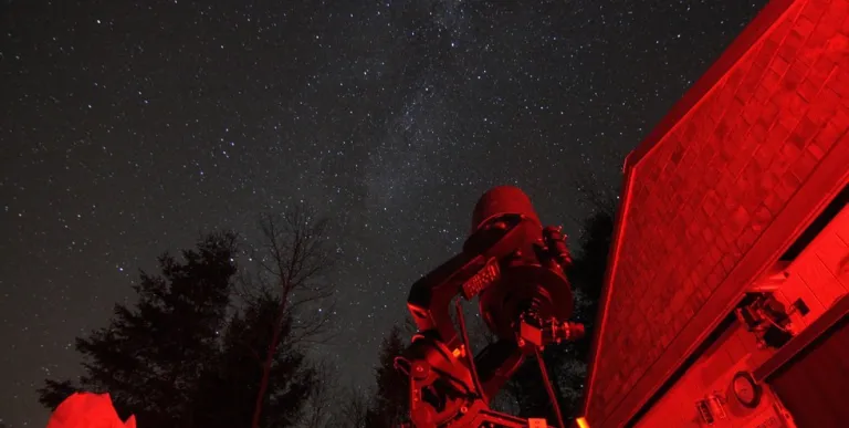 A telescope looks up at the stars&#44; glowing with red light