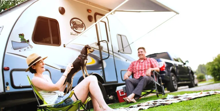People smile and laugh in lawn chairs under the awning of their camper