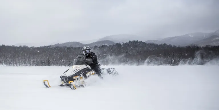 A person on a black and yellow snow machine in a field.