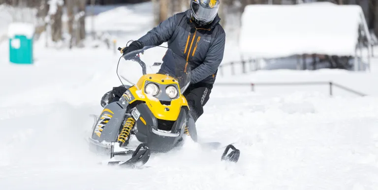 A person on a black and yellow snow machine rips through the snow.
