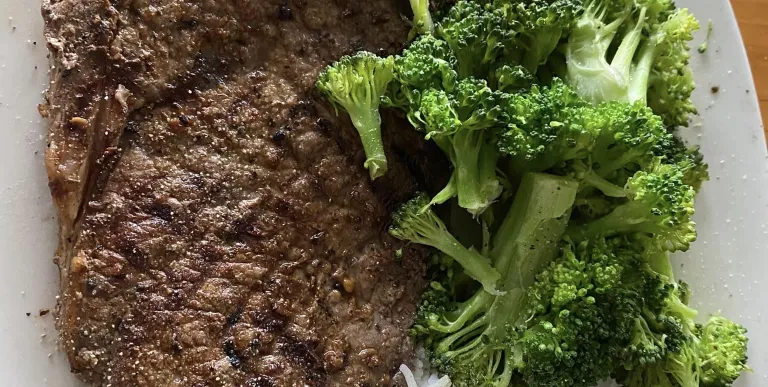 A huge steak with perfect grill crosshatches with rice and broccoli.