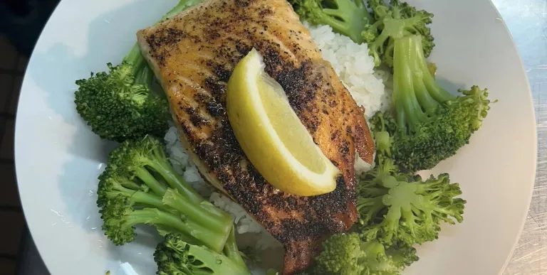 Salmon over rice with broccoli and a lemon wedge on a white plate.