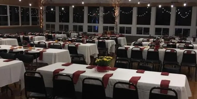 An event space set with white linen and rust accent napkins and lit with Edison string lights.