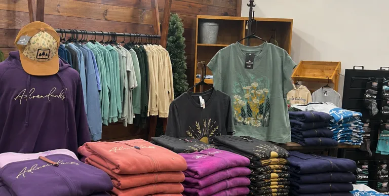 Stacks of colorful folded shirts with racks of hanging closthes.