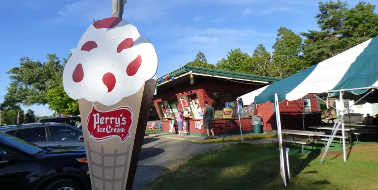 Kids sit on the arm of a giant red adirondack chair while enjoying ice cream cones.