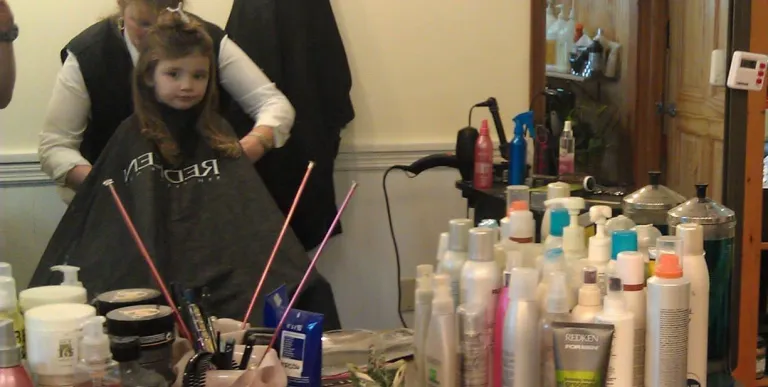 A little girl sits in the cutting chair.