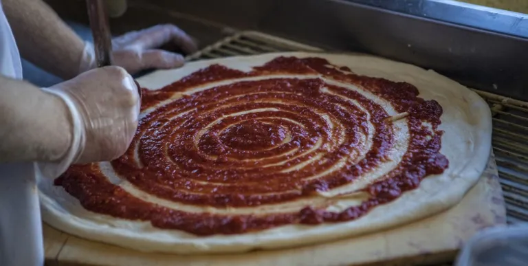 pizza dough with tomato sauce being spread on it