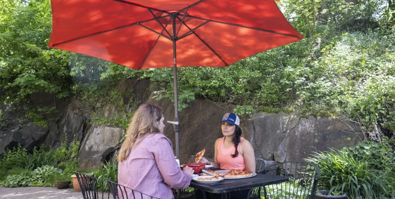 Two ladies have a meal at a metal bistro set with red umbrella