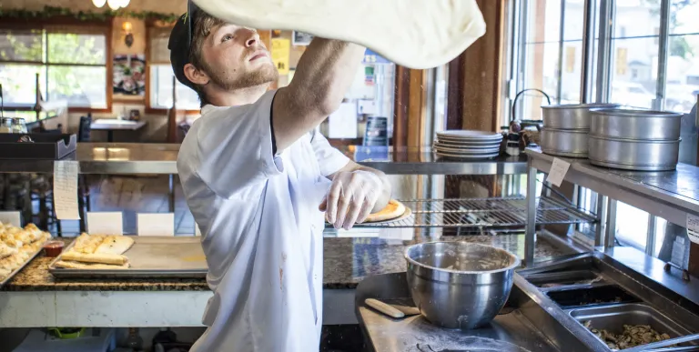 Pizza dough is being tossed above a man's head.