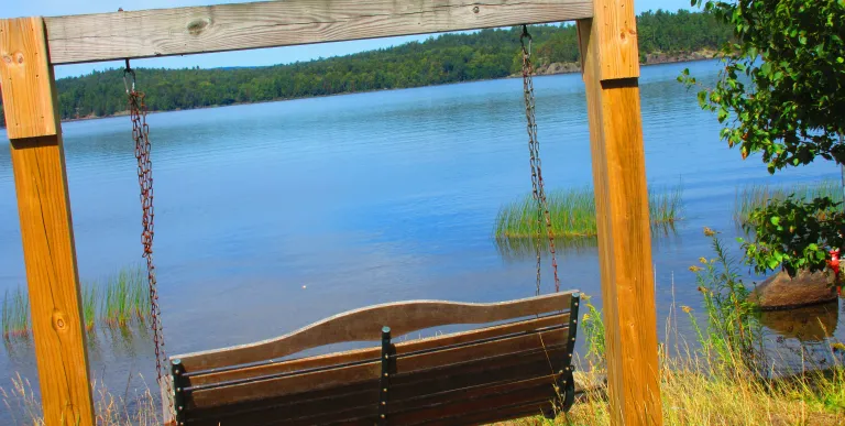 A wooden rocking bench next to the lake.
