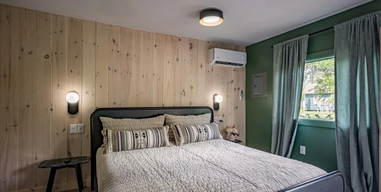 A large cream colored bed with brown striped pillows and pine walls.