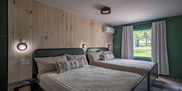A two queen room with knotty pine paneled walls behind the dark headboard.