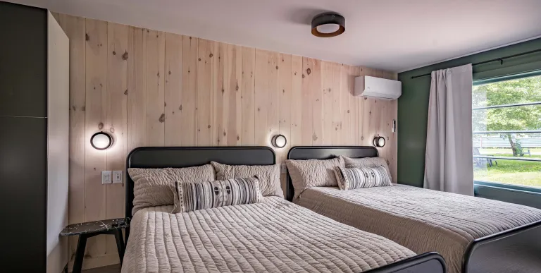 A two queen room with knotty pine paneled walls behind the dark headboard.