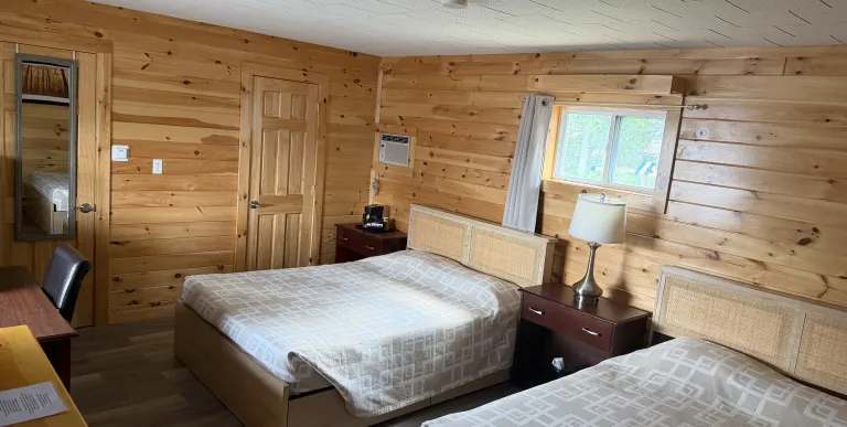 Two queen sized beds in a room with walls covered in knotty pine paneling at the Tupper Lake Motel.