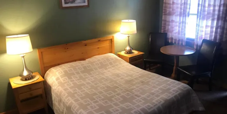 A king sized bed in a room with pine green walls at the Tupper Lake Motel.