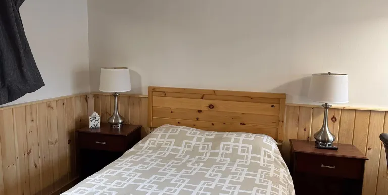 The king bed in a room with knotty pine wainscoting at the Tupper Lake Motel.